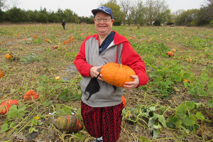 Man, smiling, standing in a pumpkin patch holding a pumpkin